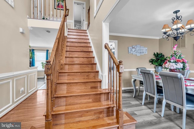 staircase featuring hardwood / wood-style flooring, crown molding, and a notable chandelier