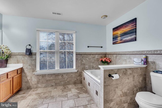 bathroom featuring tile walls, vanity, a tub, and toilet