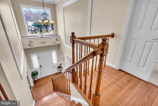 stairs featuring crown molding, hardwood / wood-style floors, and an inviting chandelier