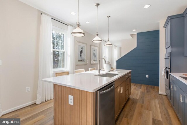 kitchen with sink, light hardwood / wood-style floors, an island with sink, and appliances with stainless steel finishes