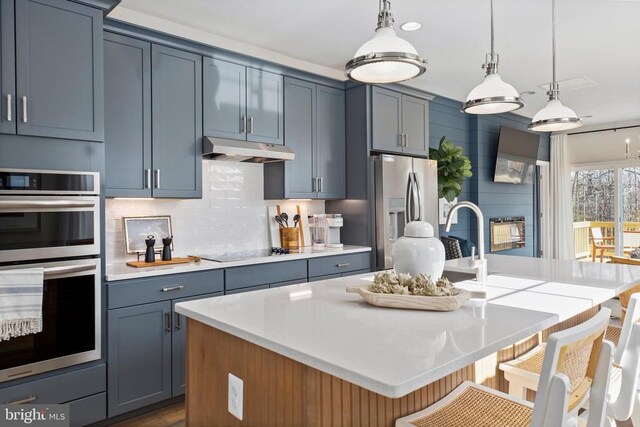 kitchen with stainless steel appliances, decorative light fixtures, a center island with sink, and backsplash