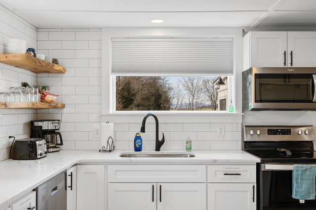 kitchen with a sink, open shelves, white cabinetry, appliances with stainless steel finishes, and decorative backsplash
