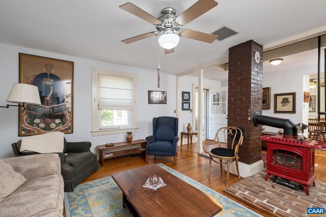 living room featuring wood-type flooring, decorative columns, ceiling fan, and a wood stove