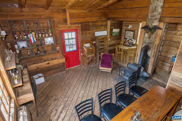 interior space with hardwood / wood-style flooring, wooden walls, beam ceiling, and a wood stove