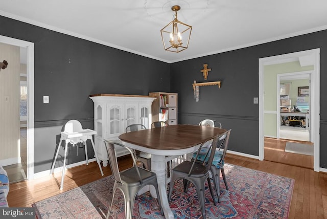 dining area featuring an inviting chandelier, crown molding, baseboards, and wood finished floors