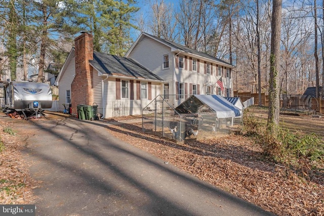 colonial-style house with a trampoline, aphalt driveway, roof with shingles, a chimney, and fence