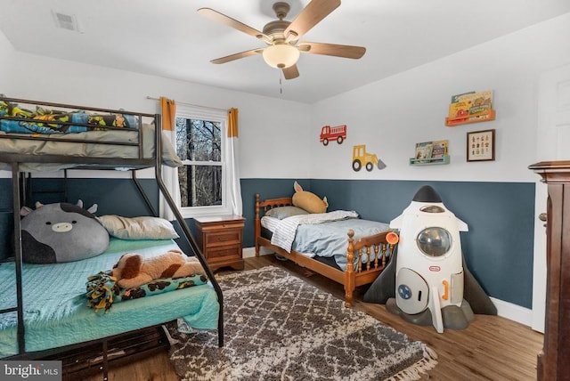 bedroom with a ceiling fan, visible vents, baseboards, and wood finished floors