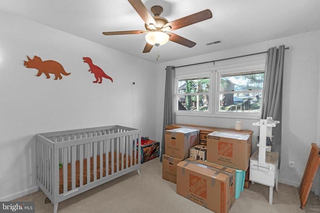 bedroom with baseboards, visible vents, a ceiling fan, light colored carpet, and a nursery area