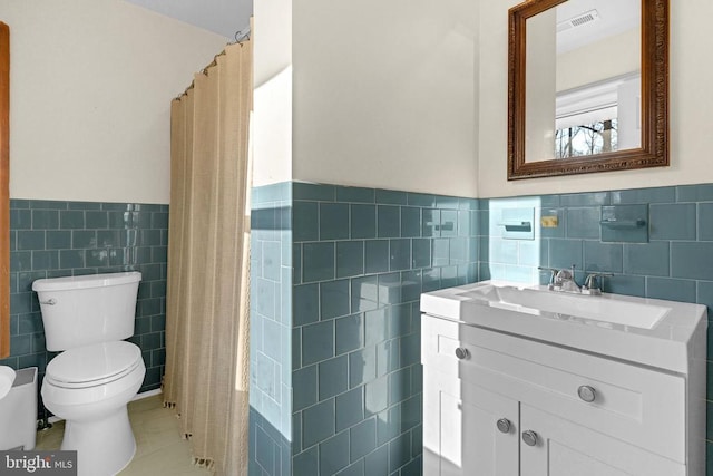 full bath featuring a wainscoted wall, tile walls, visible vents, toilet, and vanity