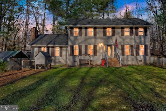 back of property at dusk with crawl space, a chimney, fence, and a lawn