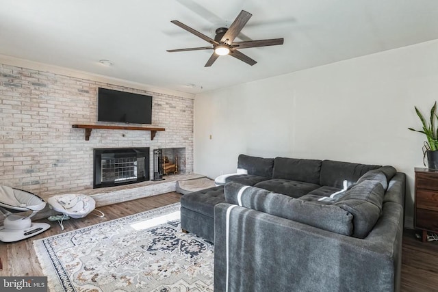 living area featuring brick wall, ceiling fan, a fireplace, and wood finished floors