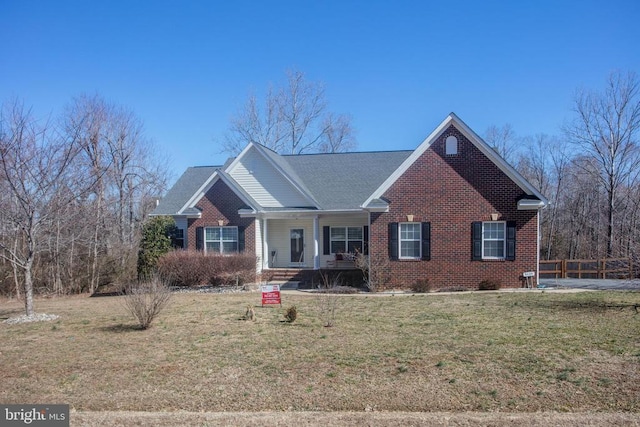 view of front facade with brick siding, covered porch, a front lawn, and fence