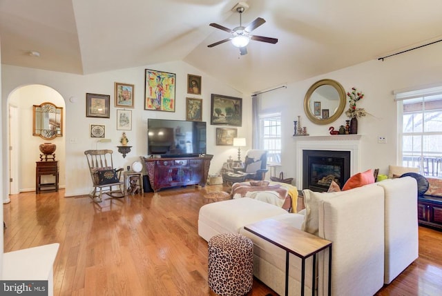 living area with ceiling fan, lofted ceiling, a glass covered fireplace, and wood finished floors