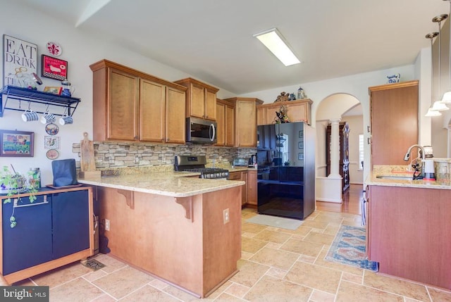 kitchen with brown cabinets, arched walkways, appliances with stainless steel finishes, a peninsula, and decorative columns