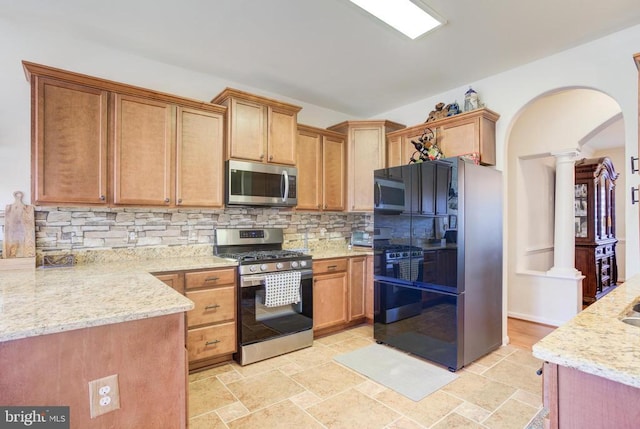 kitchen with tasteful backsplash, light stone counters, appliances with stainless steel finishes, arched walkways, and ornate columns