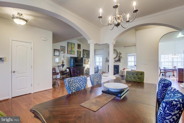 dining space featuring a notable chandelier, wood finished floors, a fireplace, and ornamental molding