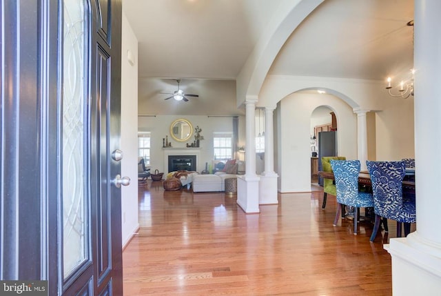 foyer entrance with ornate columns, arched walkways, a ceiling fan, and light wood finished floors