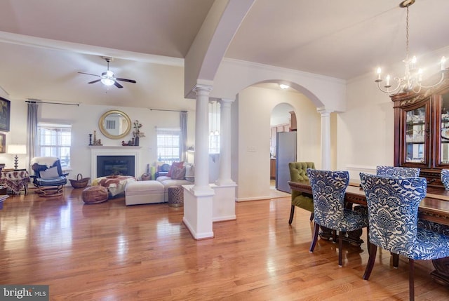 dining room featuring arched walkways, a healthy amount of sunlight, light wood-style flooring, and ceiling fan with notable chandelier