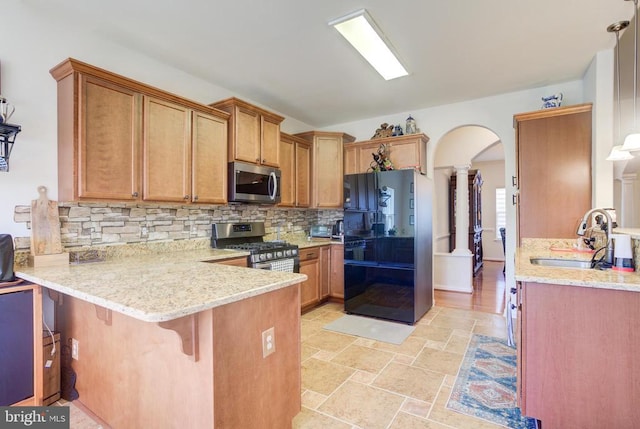 kitchen featuring a peninsula, decorative columns, a sink, appliances with stainless steel finishes, and tasteful backsplash