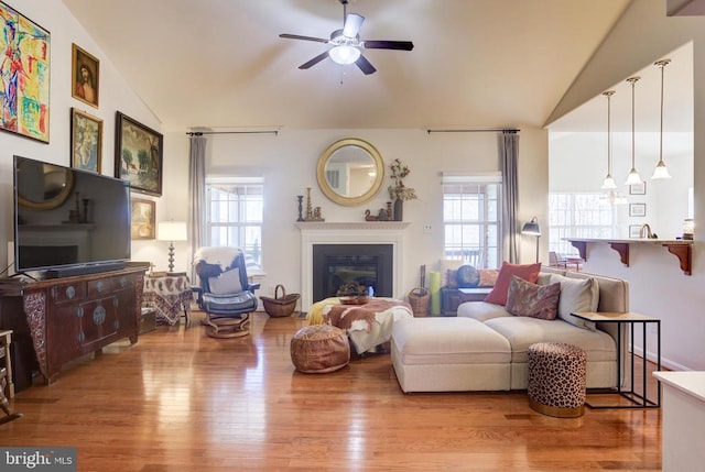 living room featuring wood finished floors, lofted ceiling, plenty of natural light, and a glass covered fireplace