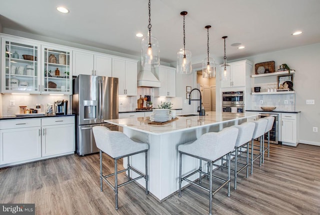 kitchen featuring open shelves, appliances with stainless steel finishes, white cabinets, a sink, and wood finished floors