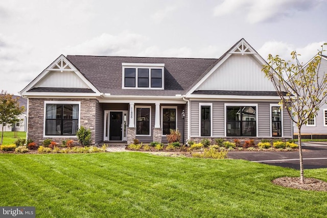 craftsman-style home with stone siding, roof with shingles, and a front lawn