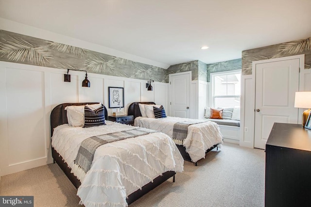 bedroom with light colored carpet, a decorative wall, and wallpapered walls