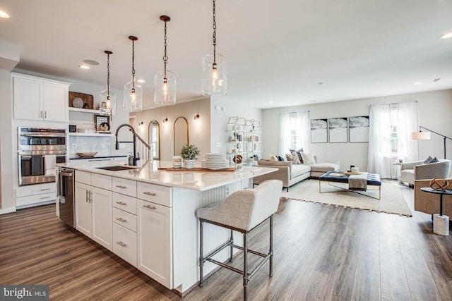 kitchen with open floor plan, double oven, dark wood-style flooring, and a sink