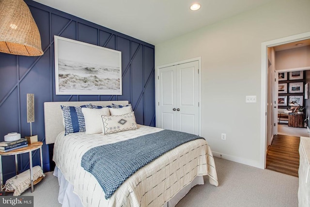 bedroom with recessed lighting, a decorative wall, carpet floors, baseboards, and a closet