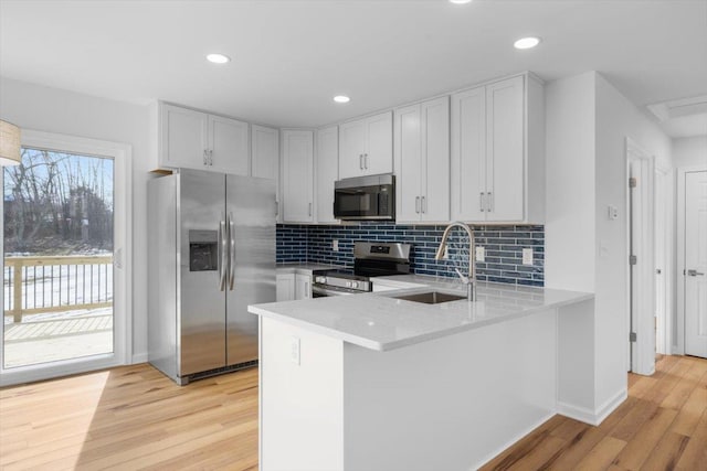 kitchen featuring white cabinetry, sink, kitchen peninsula, stainless steel appliances, and light hardwood / wood-style flooring