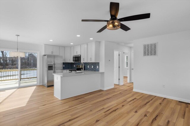 kitchen with light hardwood / wood-style flooring, stainless steel appliances, white cabinets, decorative light fixtures, and kitchen peninsula