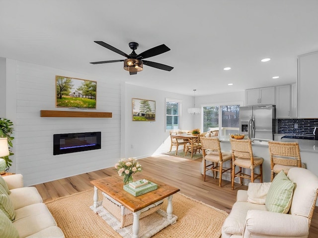 living room with ceiling fan, a large fireplace, and light wood-type flooring