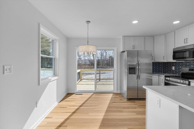 kitchen with appliances with stainless steel finishes, backsplash, a healthy amount of sunlight, decorative light fixtures, and light wood-type flooring