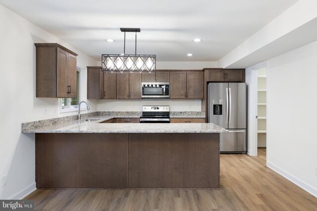 kitchen with hanging light fixtures, appliances with stainless steel finishes, dark brown cabinets, and kitchen peninsula