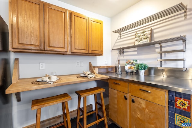 kitchen with brown cabinets, a kitchen bar, and stainless steel counters