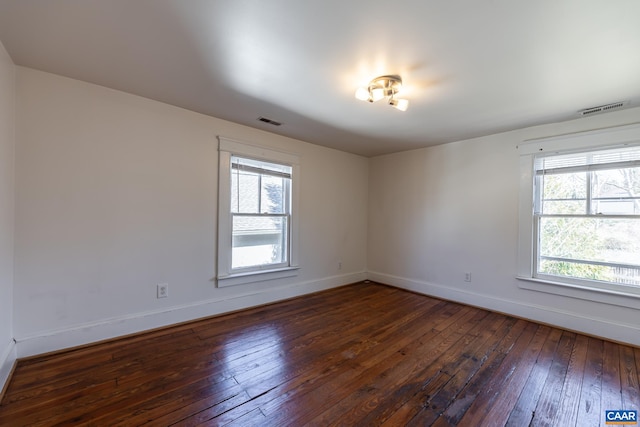 spare room with dark wood-style floors, visible vents, and baseboards