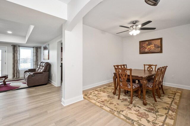 dining room with ceiling fan, a raised ceiling, and light wood-type flooring