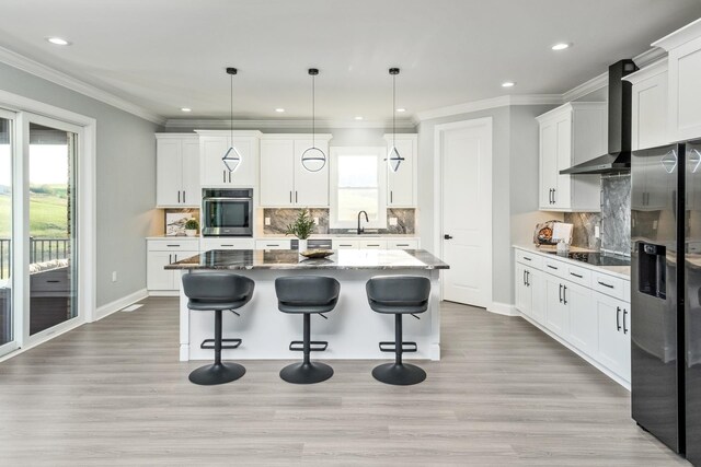 kitchen featuring hanging light fixtures, stainless steel appliances, white cabinets, a kitchen island, and wall chimney exhaust hood