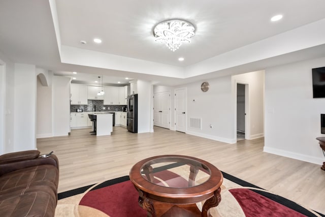 living room featuring a notable chandelier, a raised ceiling, and light wood-type flooring