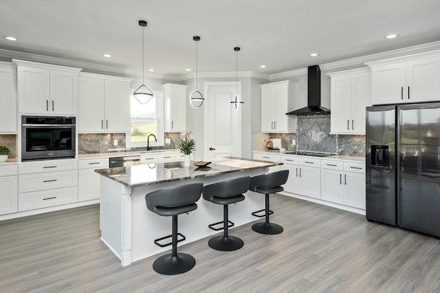 kitchen with a kitchen island, white cabinets, hanging light fixtures, black appliances, and wall chimney range hood