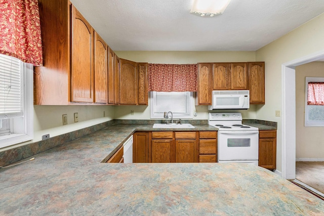 kitchen with white appliances, a sink, baseboards, brown cabinetry, and dark countertops