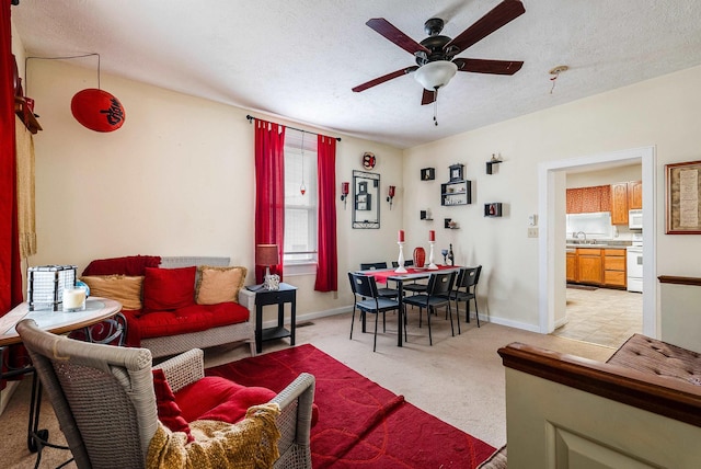 living area featuring light carpet, baseboards, a ceiling fan, and a textured ceiling