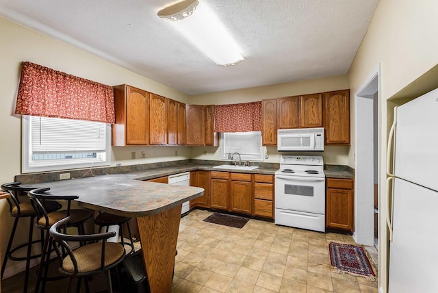 kitchen with a peninsula, white appliances, a sink, brown cabinets, and dark countertops