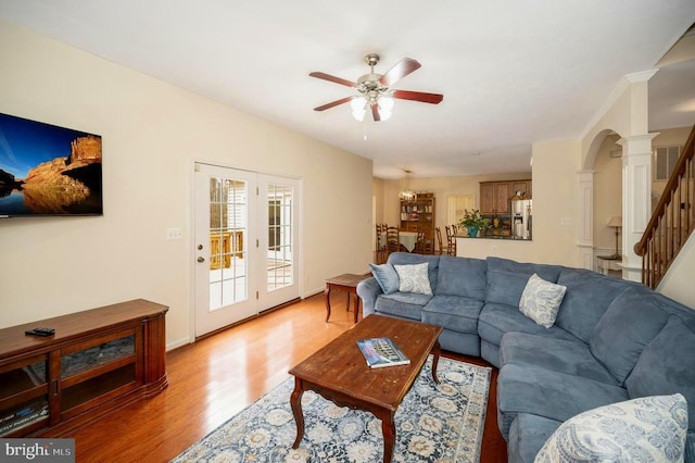 living room with arched walkways, light wood-type flooring, decorative columns, a ceiling fan, and stairs