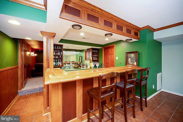 bar with indoor wet bar, baseboards, ornamental molding, tile patterned flooring, and decorative columns