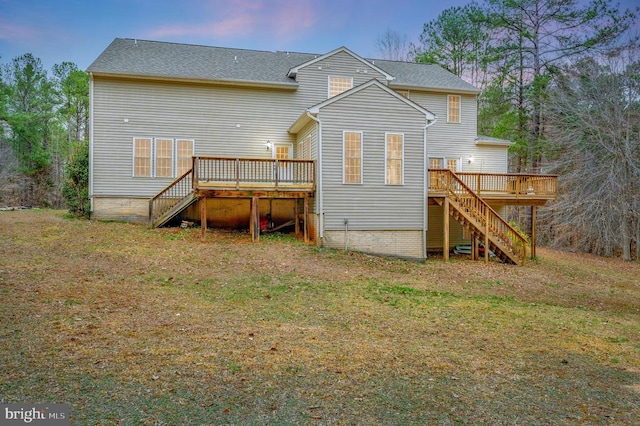 back of property at dusk featuring stairway, a lawn, and a deck
