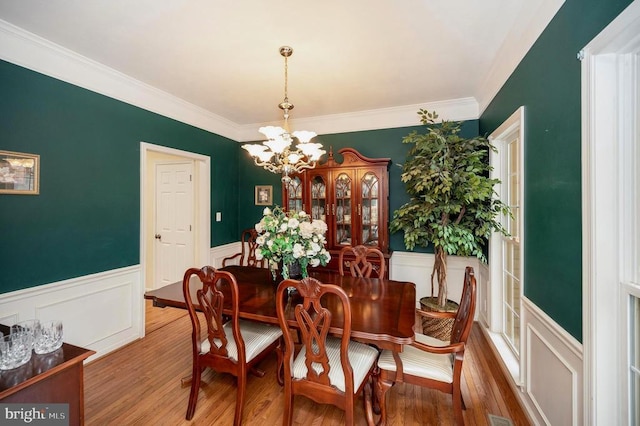 dining room with a wainscoted wall, wood finished floors, a chandelier, and crown molding