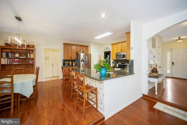 kitchen with decorative backsplash, stainless steel appliances, arched walkways, and dark wood-style flooring