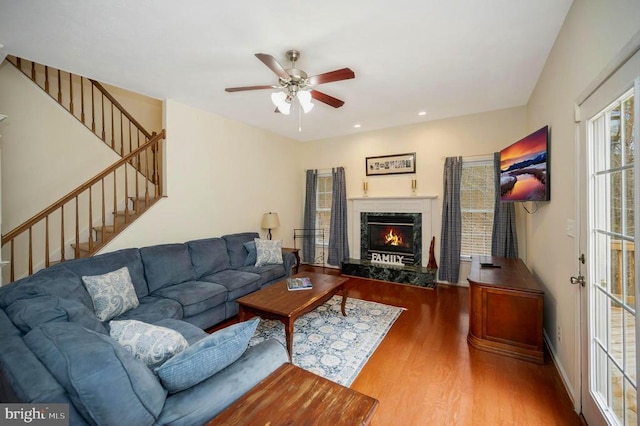 living area with a premium fireplace, wood finished floors, stairs, and ceiling fan