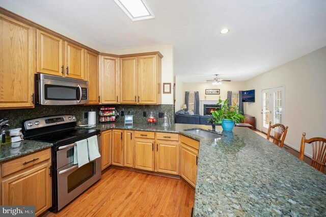 kitchen with a sink, dark stone countertops, tasteful backsplash, light wood-type flooring, and appliances with stainless steel finishes